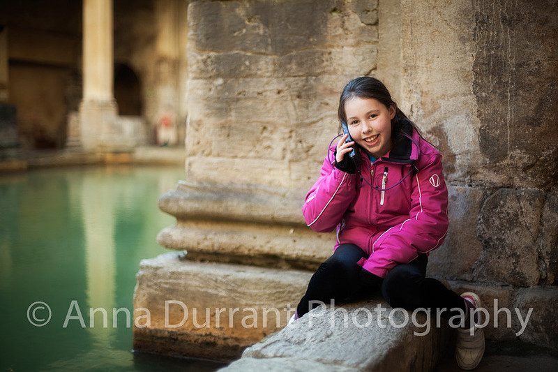 girl sitting by side of The Roman Baths in Bath